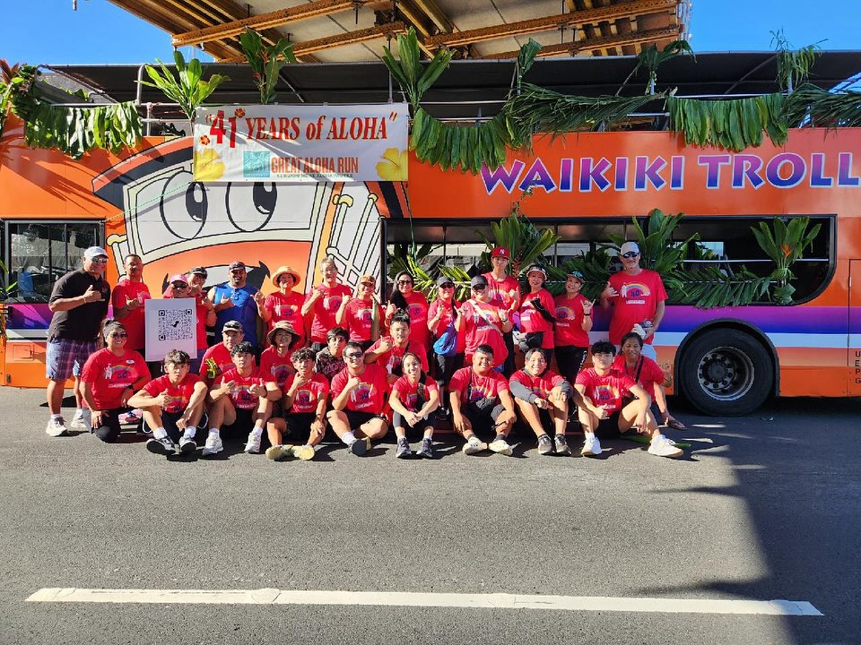 Team Great Aloha Run posing in front of the Waikiki Trolley which is decked out in tropical ti leaf.