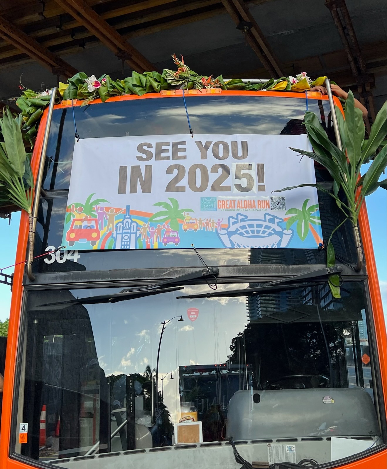 A colorful banner that says "See You in 2025 !" hangs on the front of the Wakiki Trolley, surrounded by ti leaf.